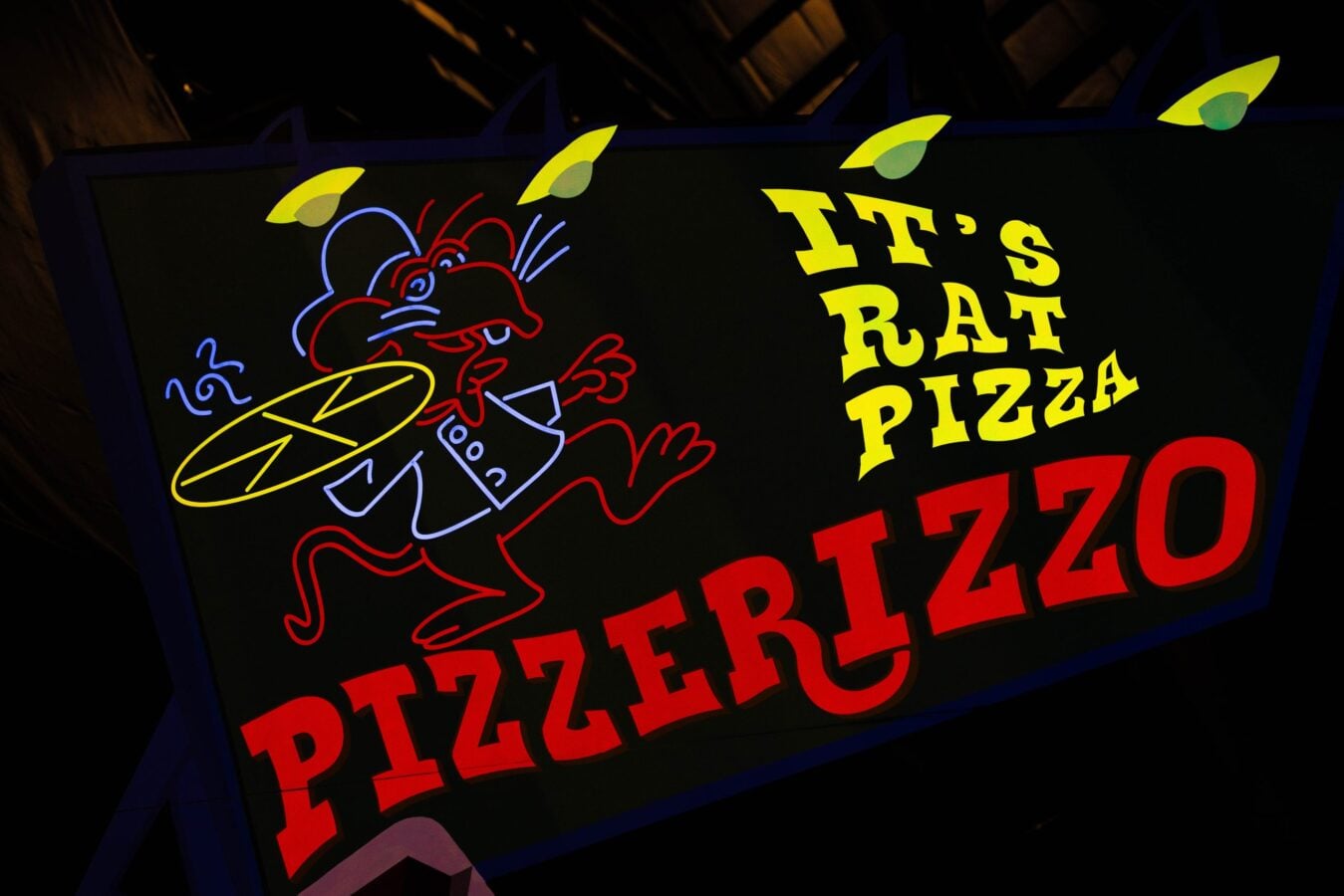 Neon sign showing a red cartoon rat holding a pizza slice with bright yellow text that reads ITS PIZZA on a dark background