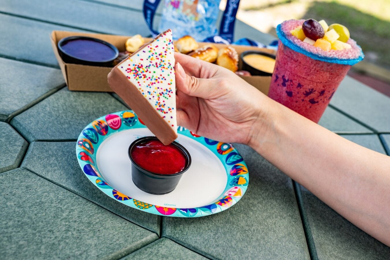 Hand holding a white frosted triangle cookie with colorful sprinkles at an outdoor picnic table