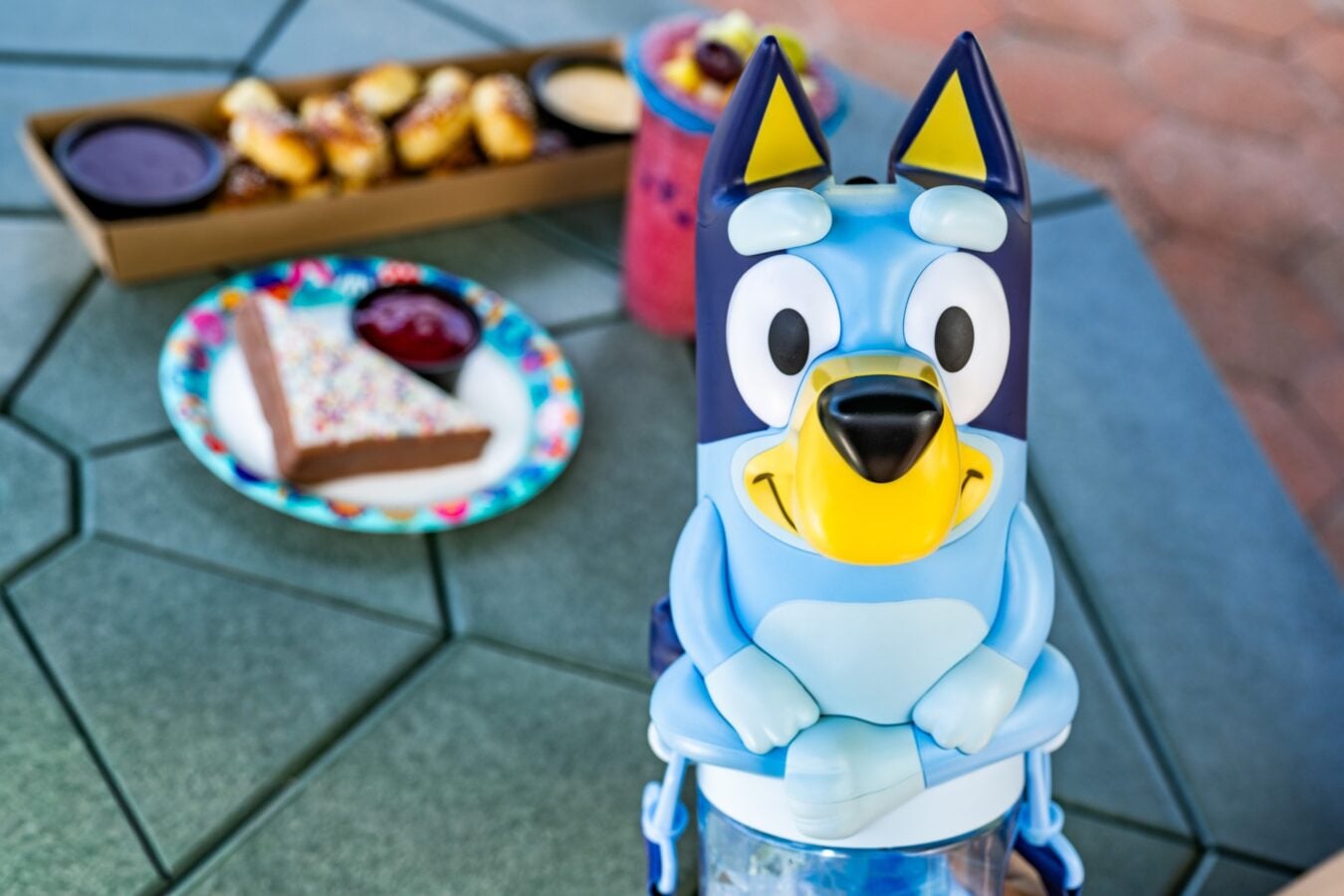 Close up of a blue cartoon ride on toy with a yellow beak at a birthday party with cake and snacks in the background