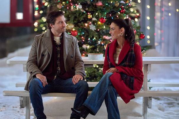 6a19bca05e852 Fantasy Land News A man and woman sit on a white wooden bench outside talking by a decorated Christmas tree in a snowy setting