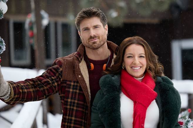 6a19bca07f247 Fantasy Land News Smiling couple posing outdoors in winter snow man in a plaid jacket with a knit collar and headphones woman in a green coat with a bright red scarf