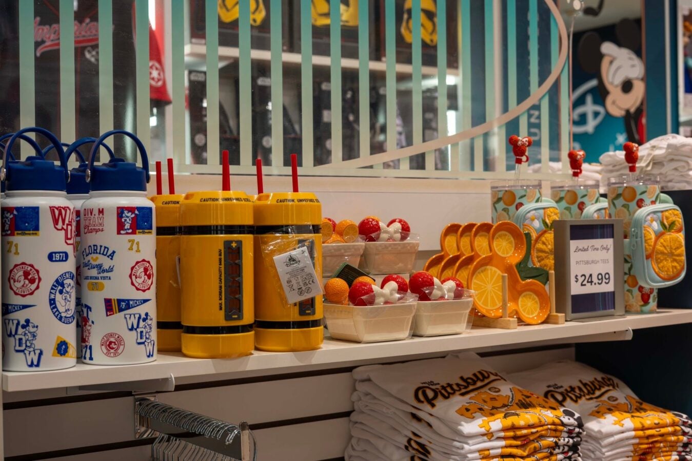 70402106217443815565405134675685496319359961n Fantasy Land News Disney themed souvenir display white water bottles with blue caps and yellow insulated cups on a store shelf plus orange slice shaped dishes in front