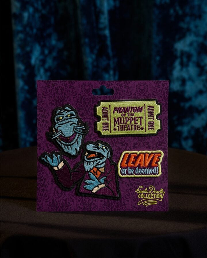 Purple display card featuring embroidered Muppet patches on a patterned backdrop including a Phantom of the Muppet Theatre badge and a Leave or be doomed patch with Uncle Deadly Collection logo