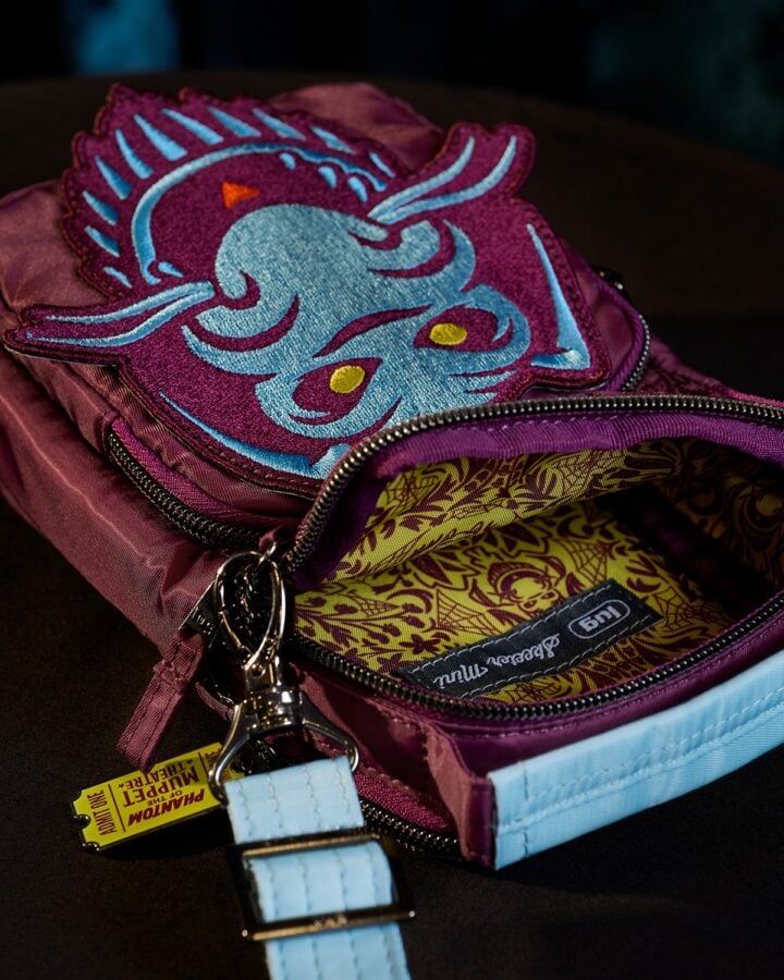Purple backpack with a blue dragon patch on the front zipper open to reveal a yellow patterned lining and light blue strap details on a dark surface