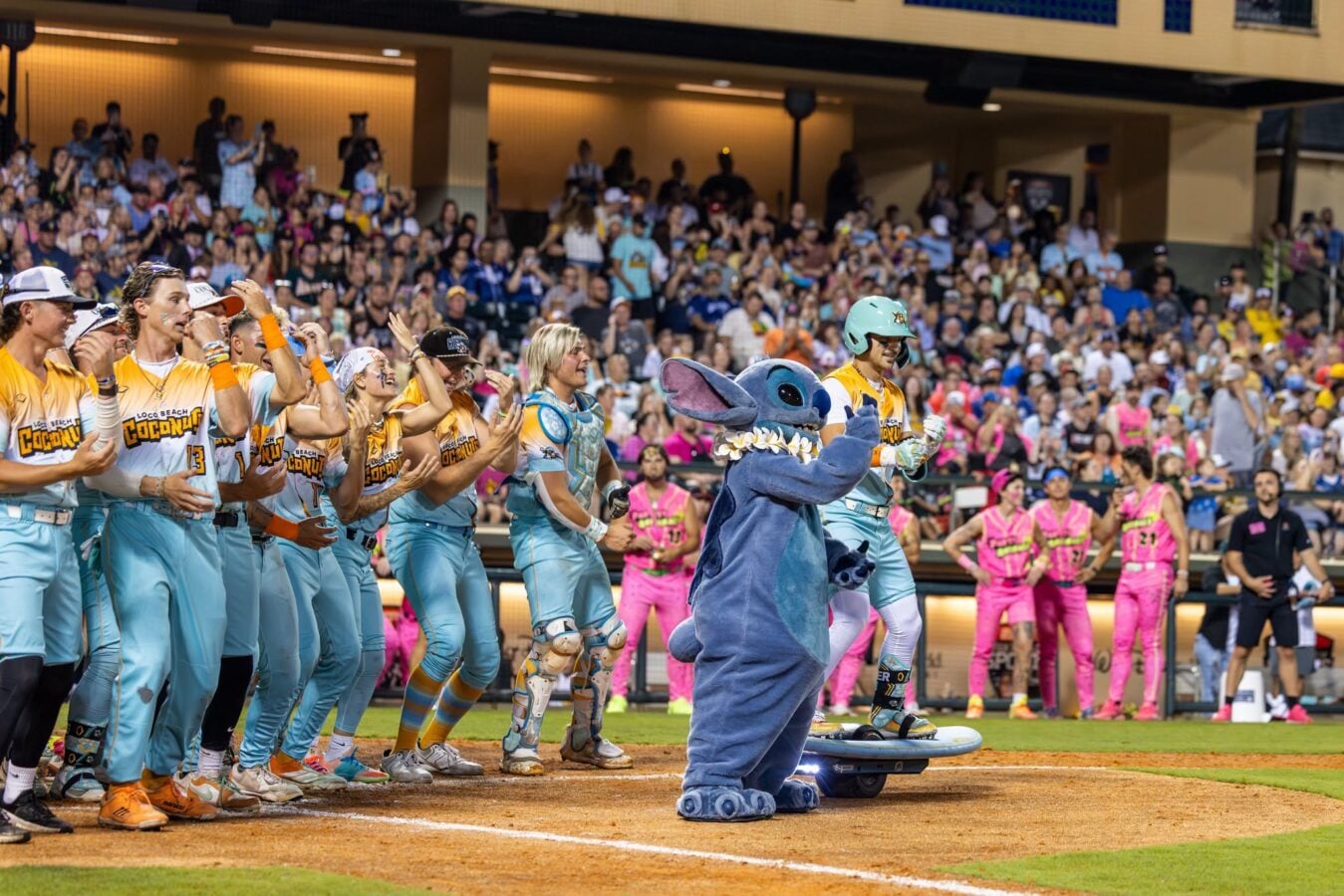 Line of players in turquoise uniforms cheering at a sports field crowd watching from stands in the background a blue elephant mascot in the foreground