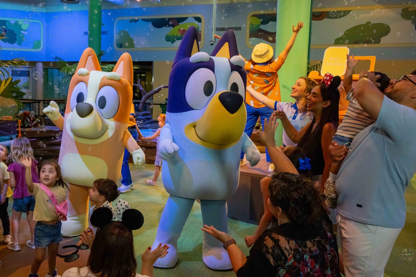 Children and adults reach out to friendly blue and orange cartoon dogs during a bubbly character meet and greet