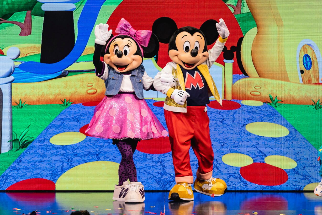 Minnie Mouse and Mickey Mouse in bright costumes wave on a colorful stage with a cartoon backdrop at a kids show stage entrance