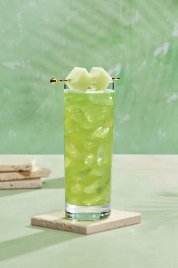 Honeydew Smash Fantasy Land News Tall glass of green iced drink with melon wedges on a skewer resting on the rim