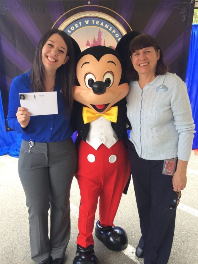Two women pose with a life size Mickey Mouse mascot at an event smiling for the camera