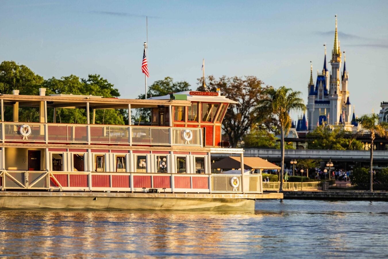 Red and white paddlewheel riverboat docked along the river with a fairytale castle visible in the background on the right