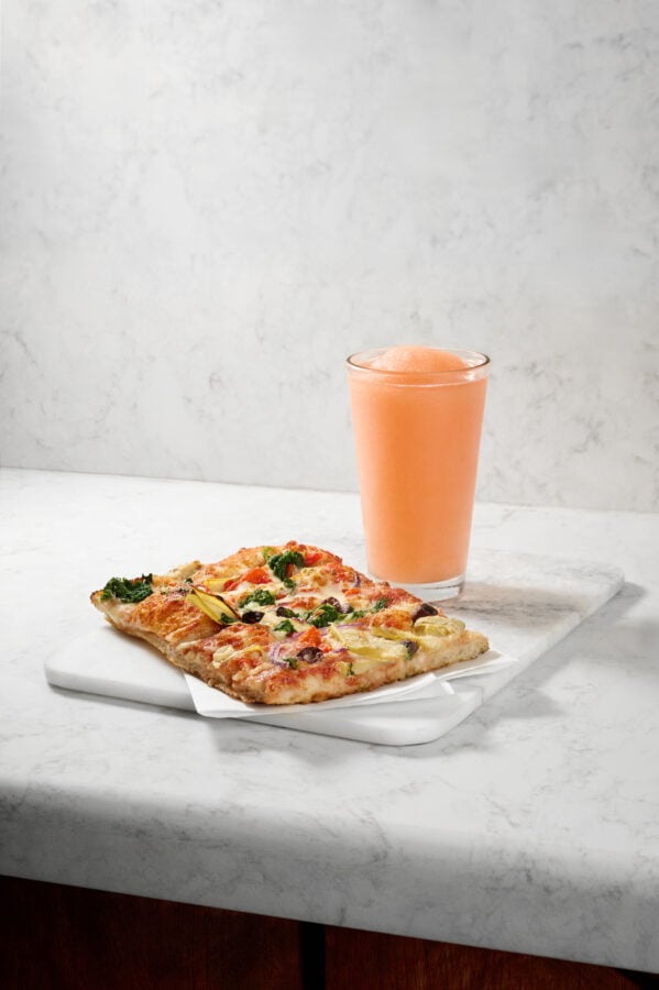 Stacked from 7 images Method=B R=8S=4 Fantasy Land News Two slices of veggie pizza on a marble board with a tall glass of pink orange juice in the background