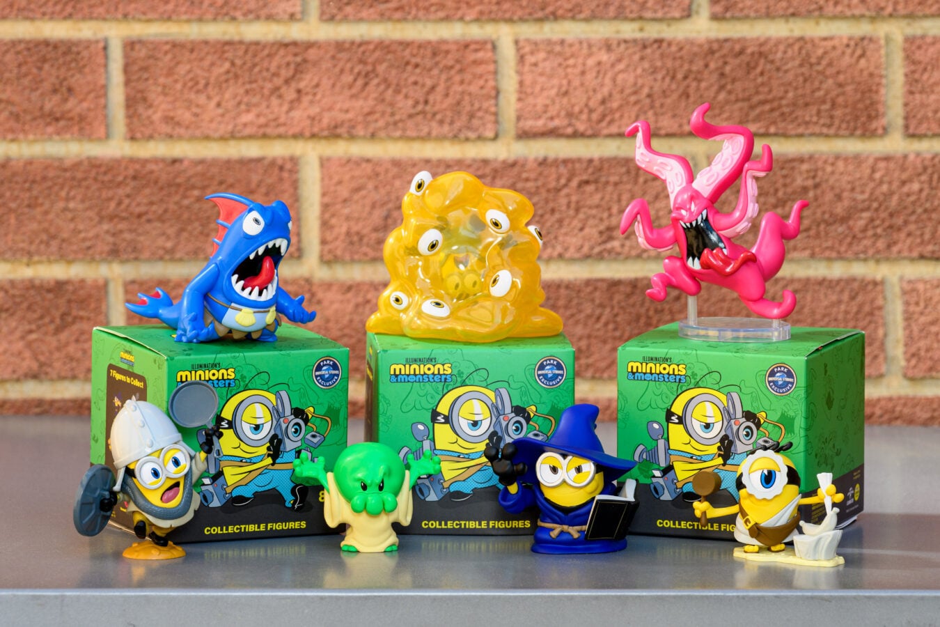 Colorful Minions and monsters toy figures arranged on green display boxes in front of a brick wall