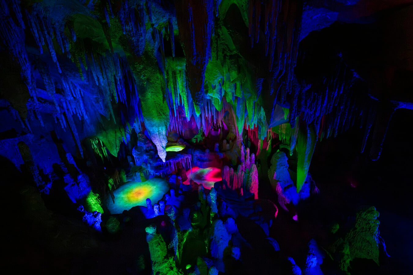 Inside a dark cave with hanging stalactites illuminated by blue green and pink lights