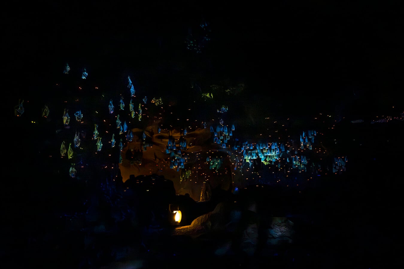 Night scene with numerous blue glowing paper lanterns hanging above a dark rocky ground
