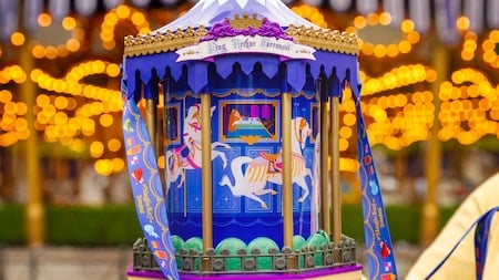 Close up of a blue ornate carousel with gold trim and painted horses warm festival lights in the background