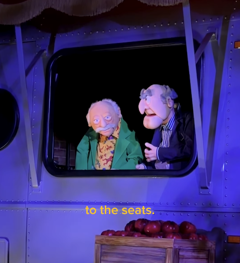Two elderly puppet characters look out from a bus window at night with a crate of apples in view on the ledge caption reads to the seats on screen