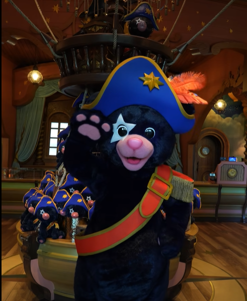 Screenshot 20260518 130311 Fantasy Land News Black plush cat in a blue pirate hat with a gold star waves from a pirate ship ride wearing a red sash and belt