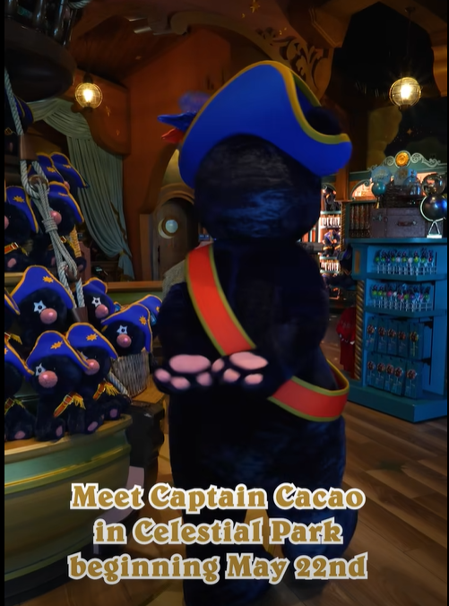 Screenshot 20260518 130327 Fantasy Land News Back view of a blue pirate cap plush with a blue hat and red yellow sash in a colorful shop overlay text reads Meet Captain Cacao in Celestial Park beginning May 22nd