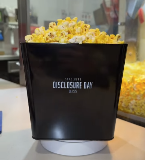 Screenshot 20260527 080803 Fantasy Land News Black square popcorn bucket overflowing with yellow popcorn on a white stand with Disclosure Day text visible on the front