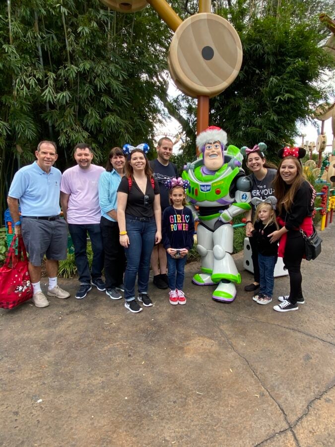 Group of adults and children posing together with a life size Buzz Lightyear character at an amusement park