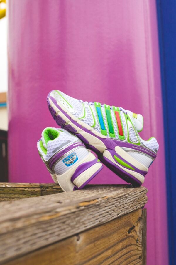 adidas x Toy Story 4 Fantasy Land News Colorful athletic sneakers stacked on a weathered wooden surface with a pink background behind them showcasing bright green and purple accents