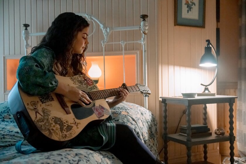 download 10 Fantasy Land News Young woman sits on a bed playing a decorated acoustic guitar in a cozy warm lit bedroom