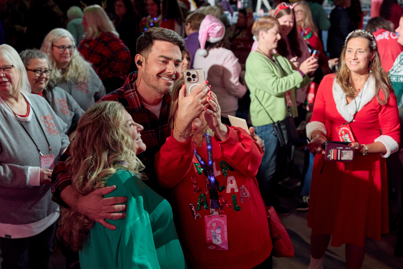 Smiling man in plaid shirt taking a selfie with a woman in a green jacket at a holiday crowd event