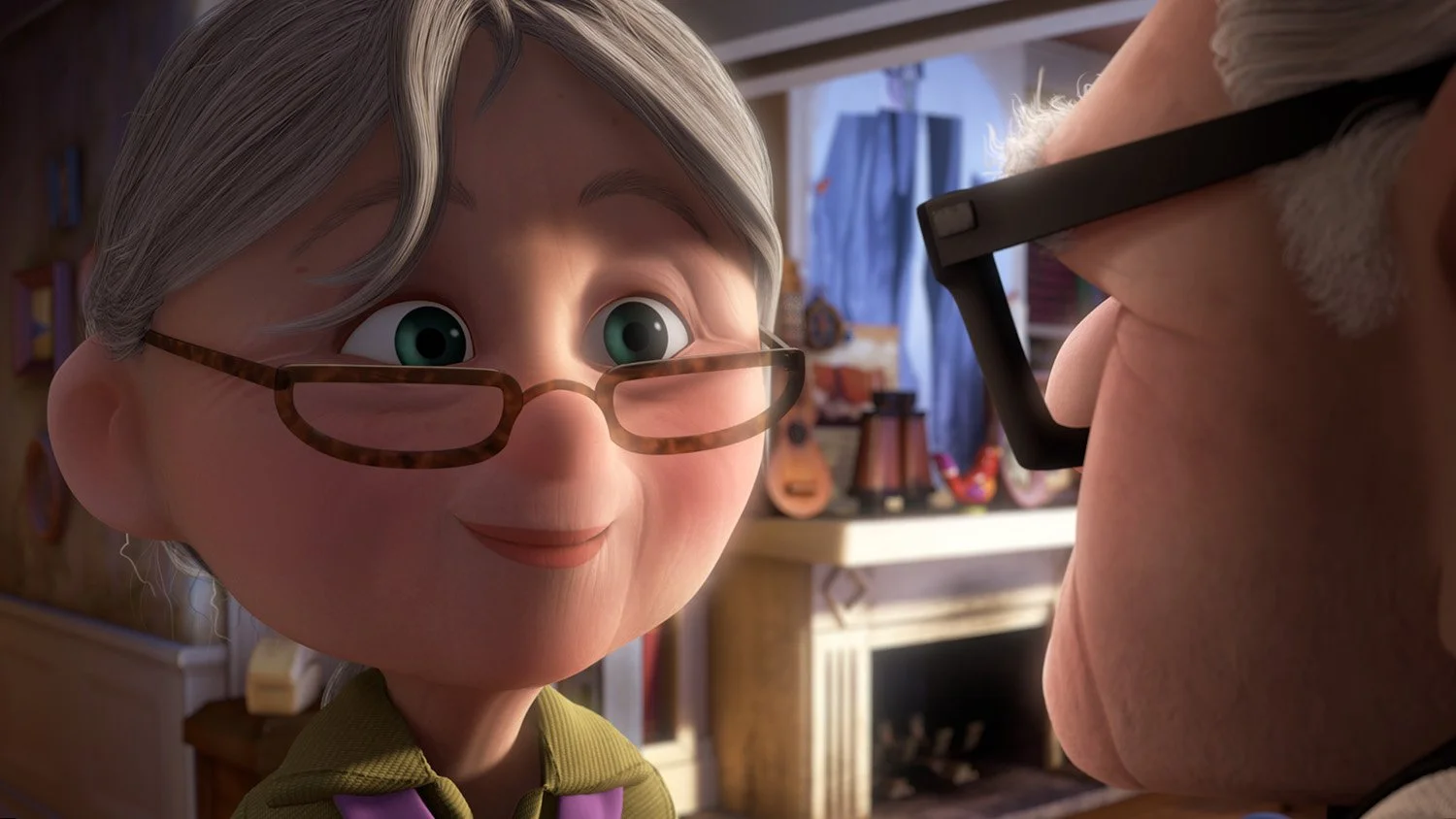 Close up of an elderly woman with gray hair and tortoiseshell glasses smiling at a man in a cozy cluttered room