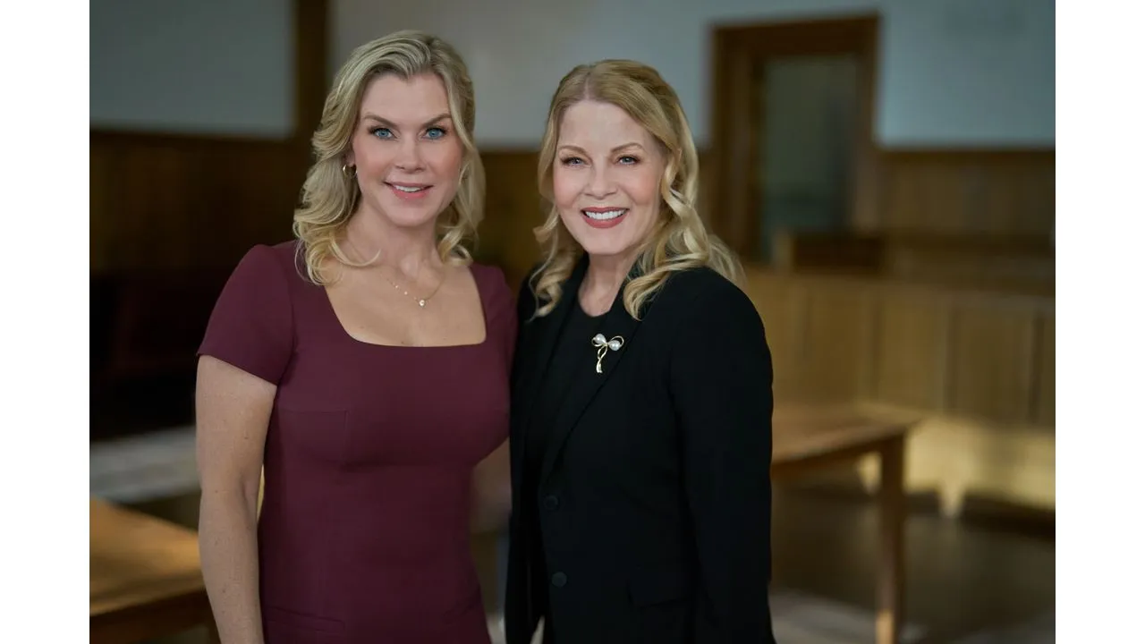 Two smiling women pose together in a wood panelled room one wears a burgundy dress the other a black blazer with a brooch