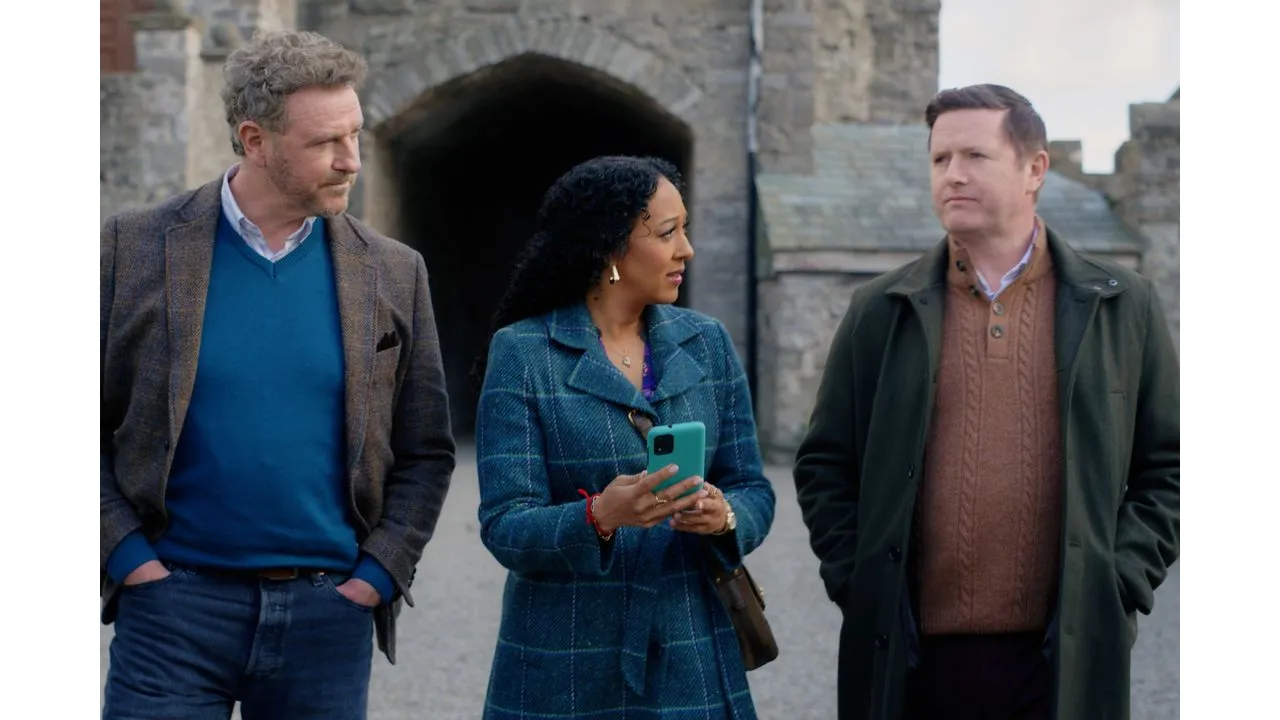Three adults walking outdoors near a stone archway woman in a blue coat holds a teal smartphone between the two men in jackets and coats