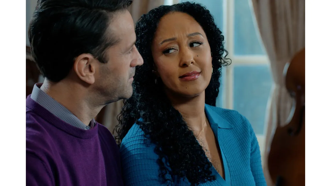 A man and a woman sit close together indoors gazing at each other as they talk by a window