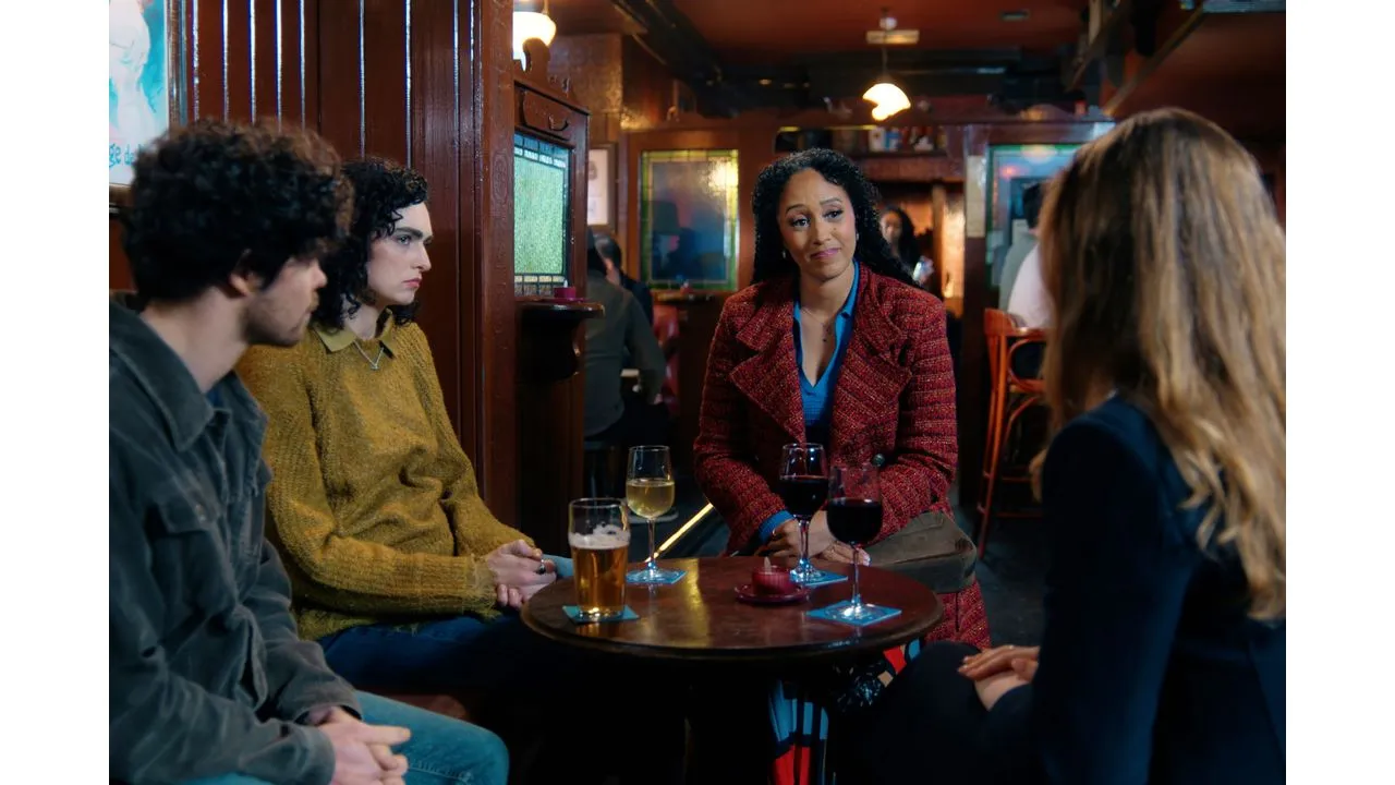 Group of four friends chatting around a round tab le at a cozy bar with drinks in front of them and a woman in a red coat speaking