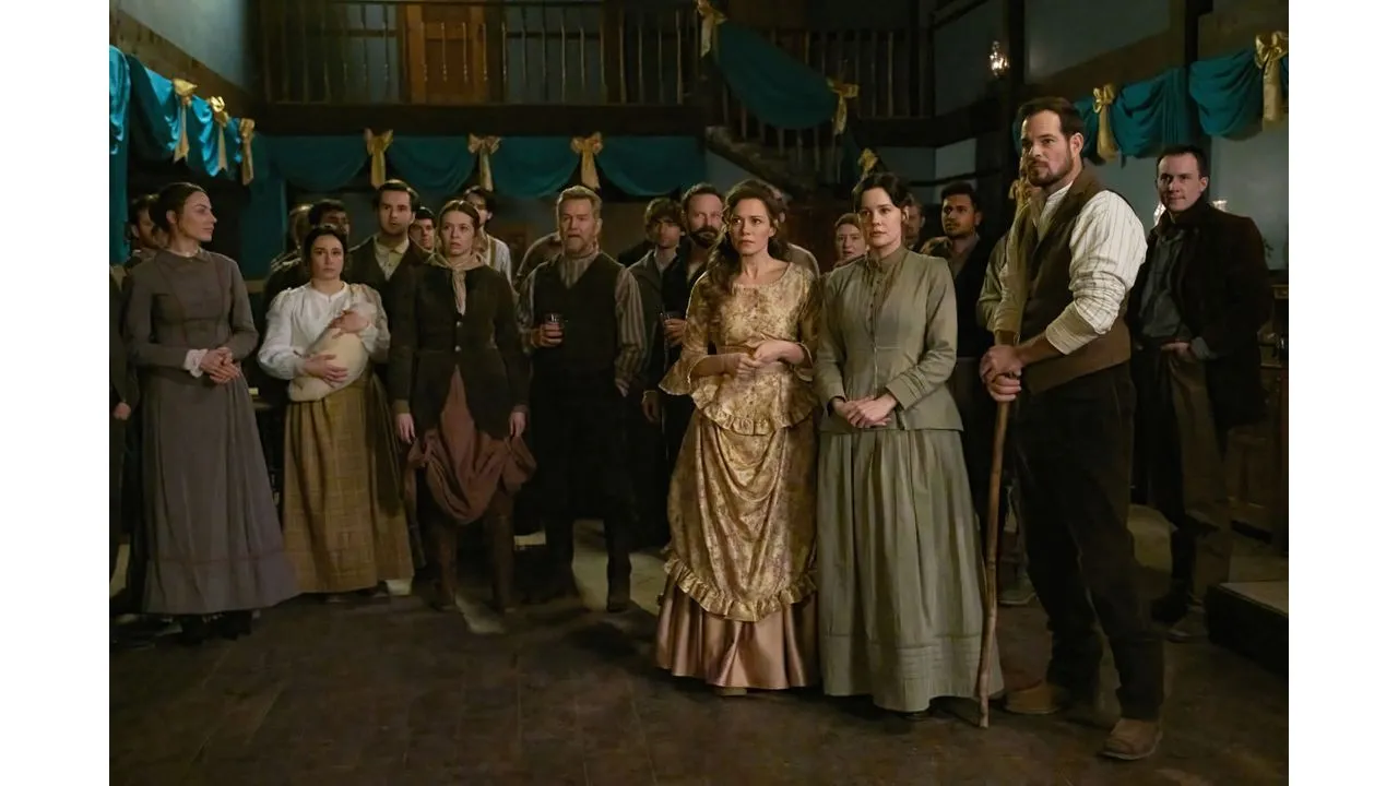 Group of people in 19th century costumes standing in a dimly lit room with teal drapery looking toward the camera suggesting a social gathering