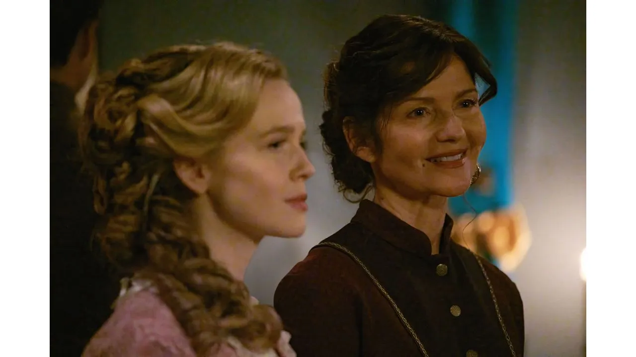 Two women in period costume smile side by side warmly lit backstage scene
