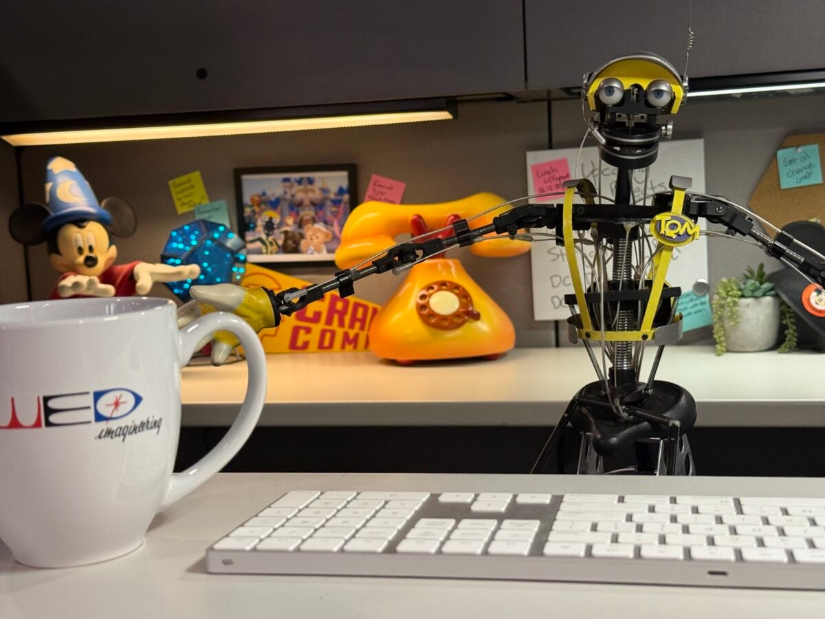 Desk scene with a white keyboard in the foreground a white mug on the left and a yellow robot figurine among colorful desk toys in the background