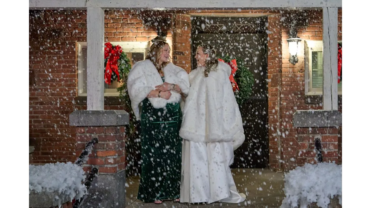 Bride in a white gown and fur wrap chats with a guest in a green dress on a snow dusted porch smiling at each other