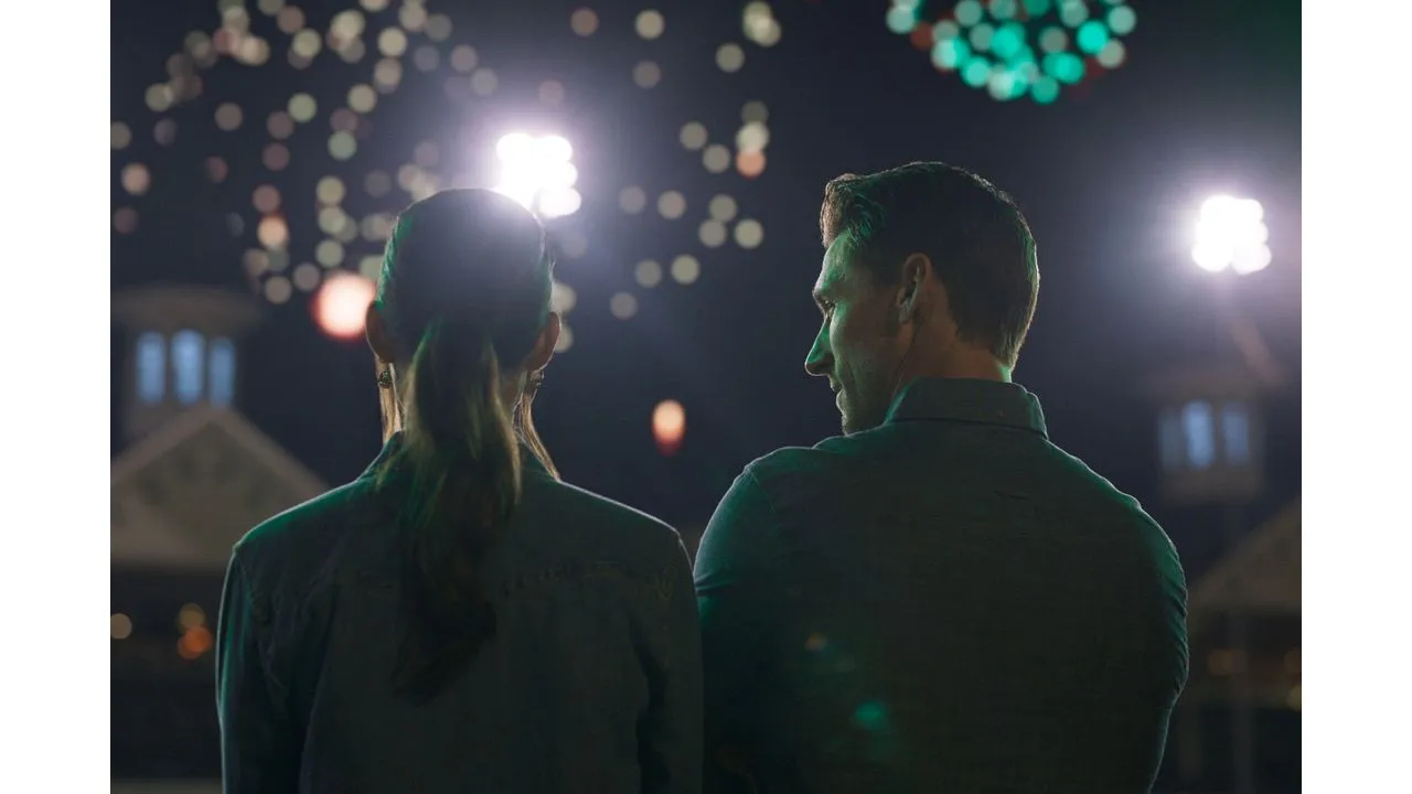 Two people stand side by side at night seen from behind watching bright bokeh lights and fireworks in the sky