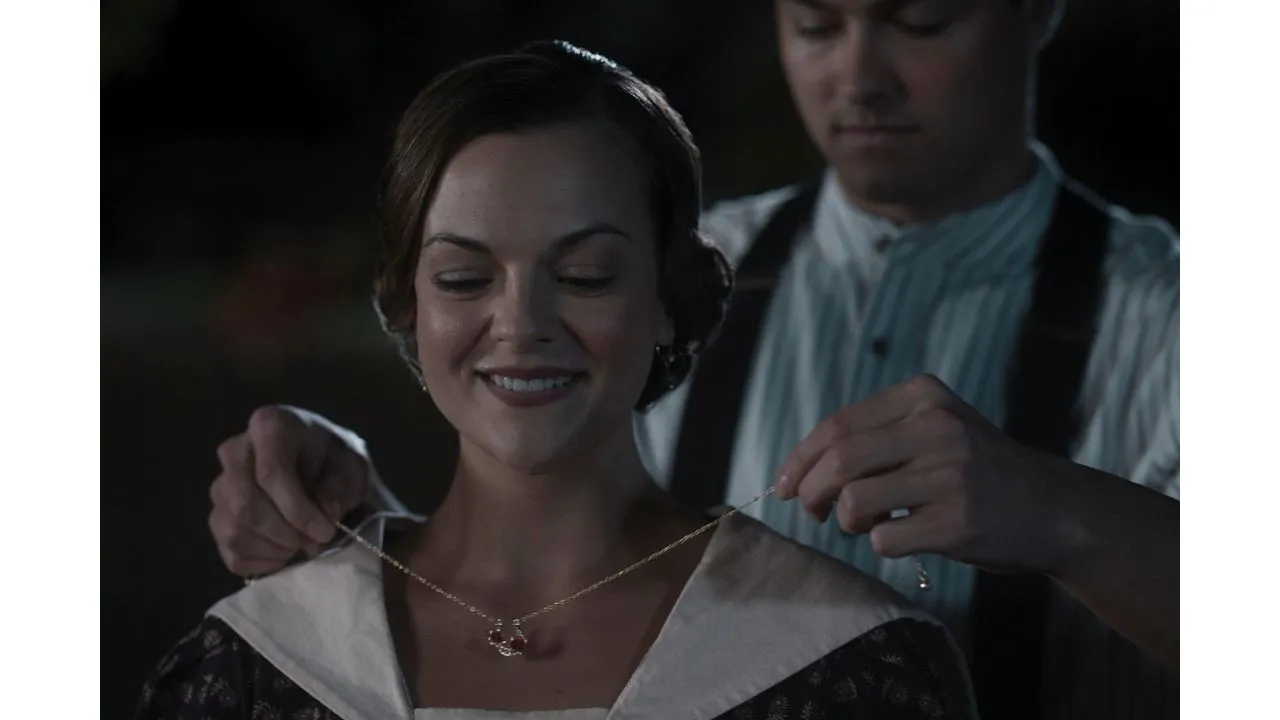 Woman smiles as a man dresses her with a delicate necklace at night outdoors