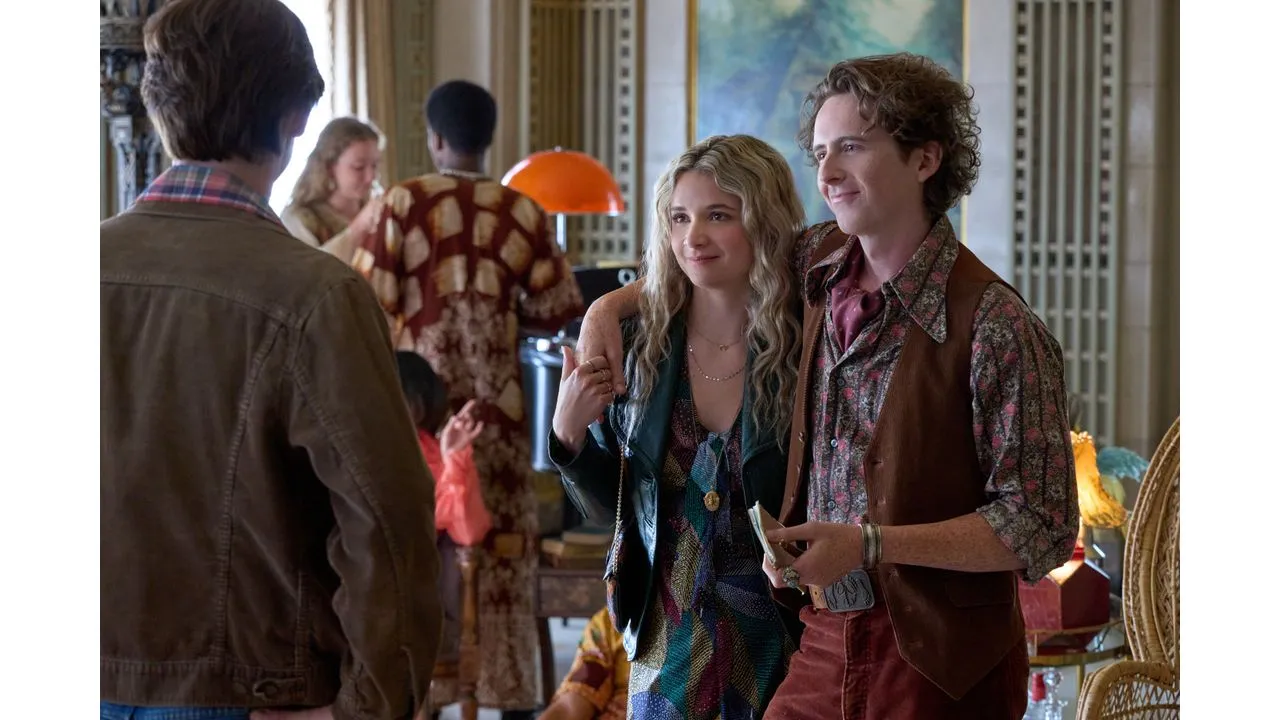 A couple in 1970s outfits poses with a friend at a retro themed party in a living room