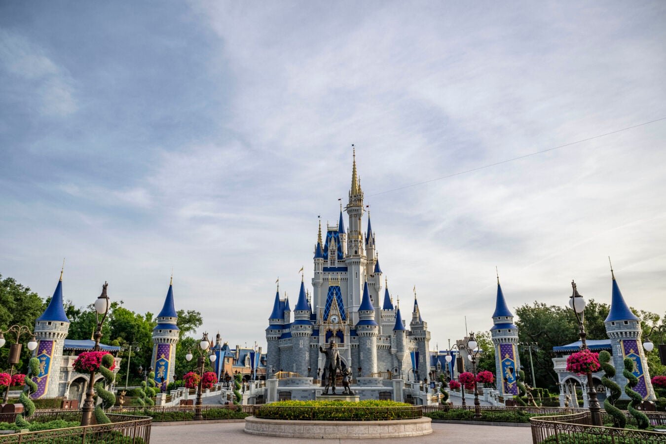 Castle with blue conical roofs and gold spires set in a landscaped park with lampposts and banners in the foreground