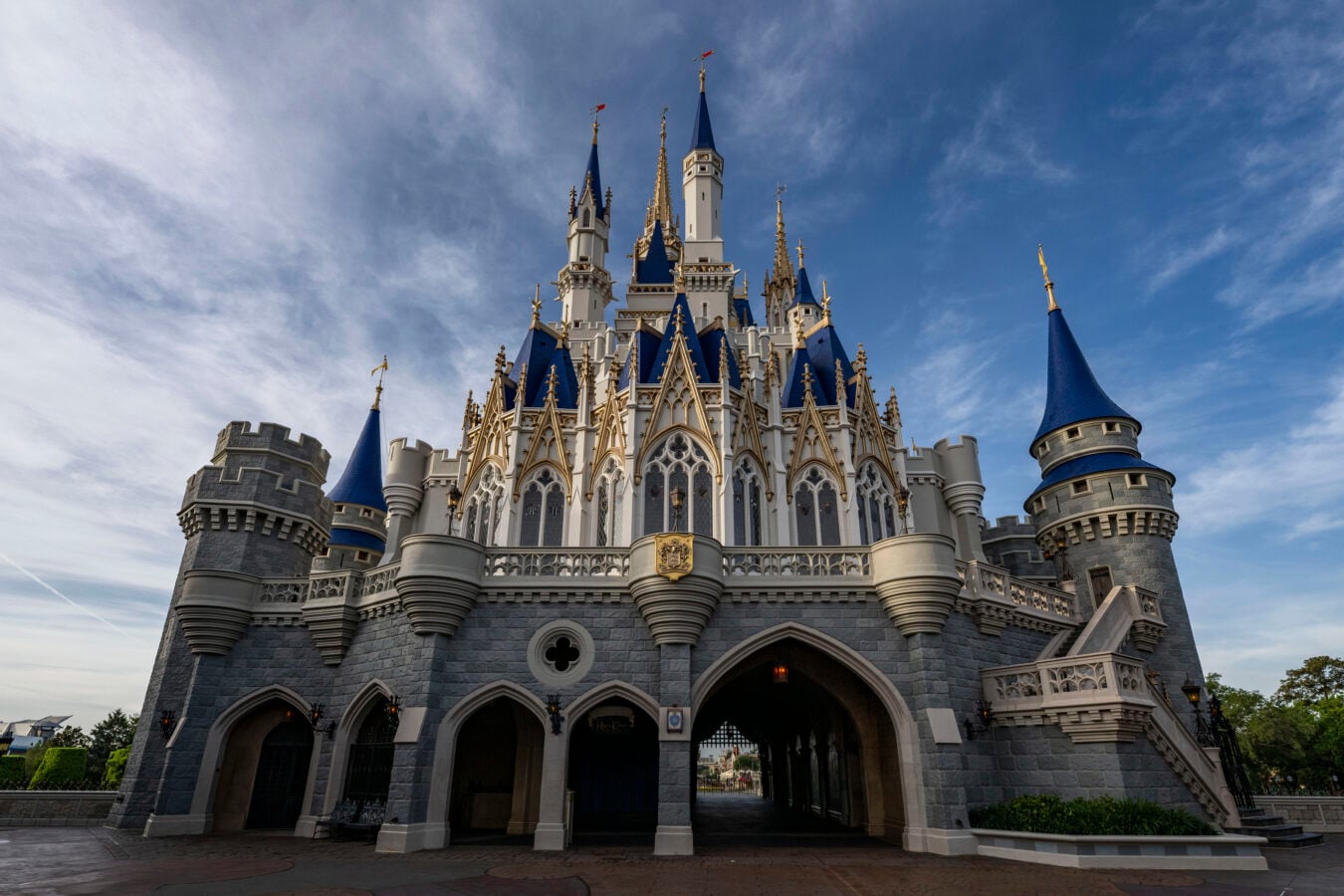 Front view of a grand fairy tale castle with blue roofs and gold spires against a blue sky at a theme park