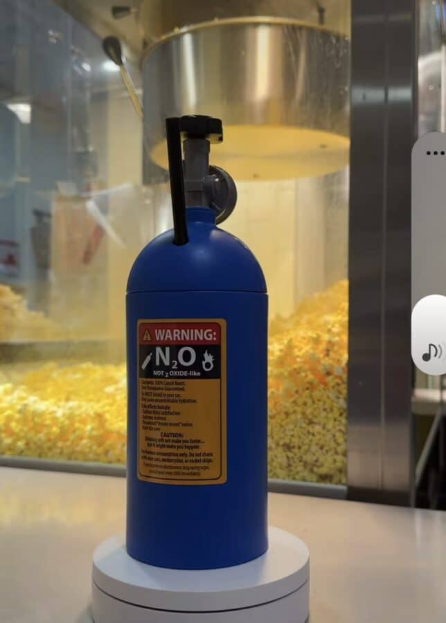 Blue nitrous oxide N2O charger canister on a display stand with a warning label visible on its front