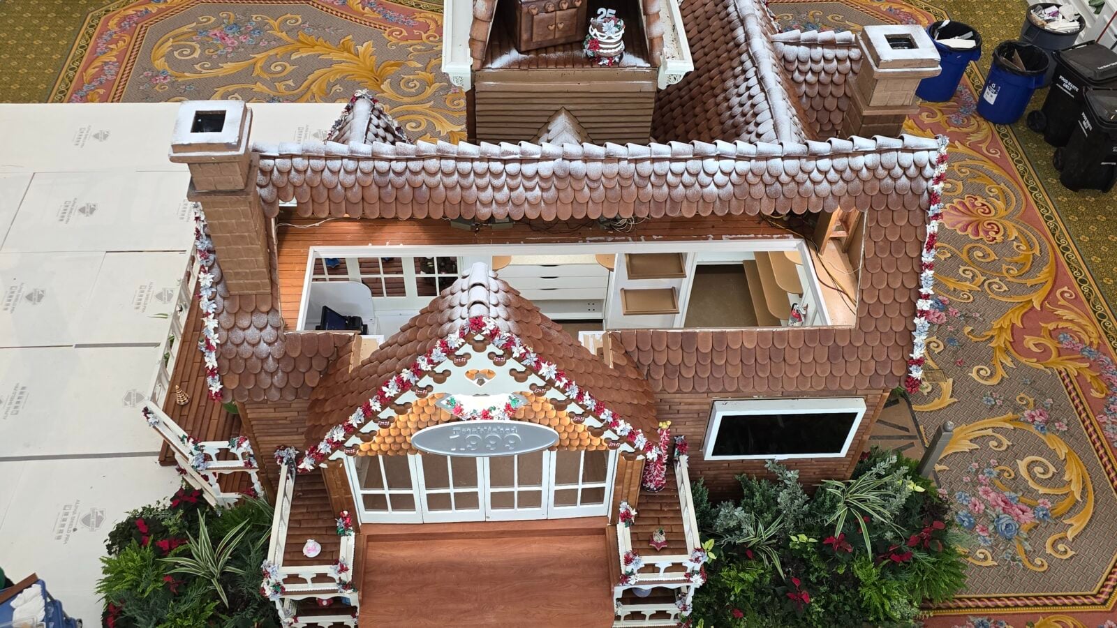 Birds eye view of a decorative wooden miniature house with a brown tile roof and white trim indoors on a patterned carpet