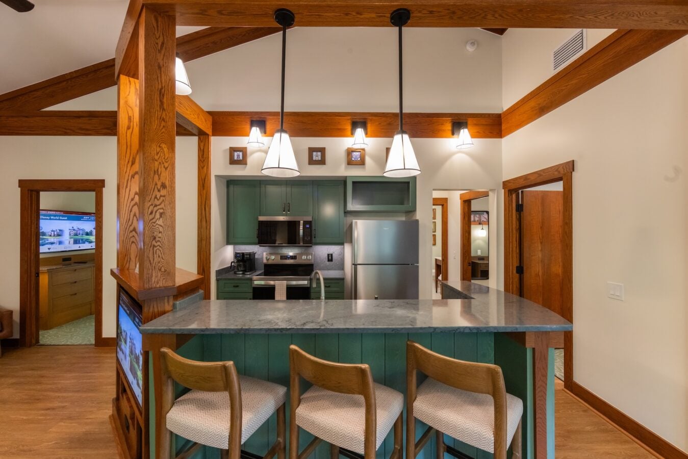 Open kitchen with green cabinets stainless steel appliances and a marble island beneath wooden beams