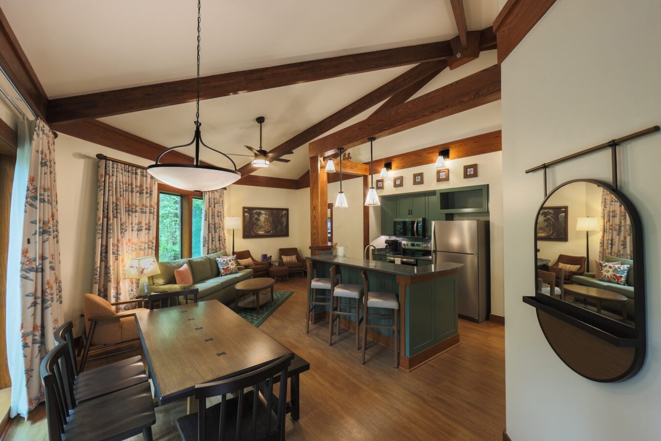 Open plan living room and kitchen with a green kitchen island stainless appliances and exposed wooden ceiling beams