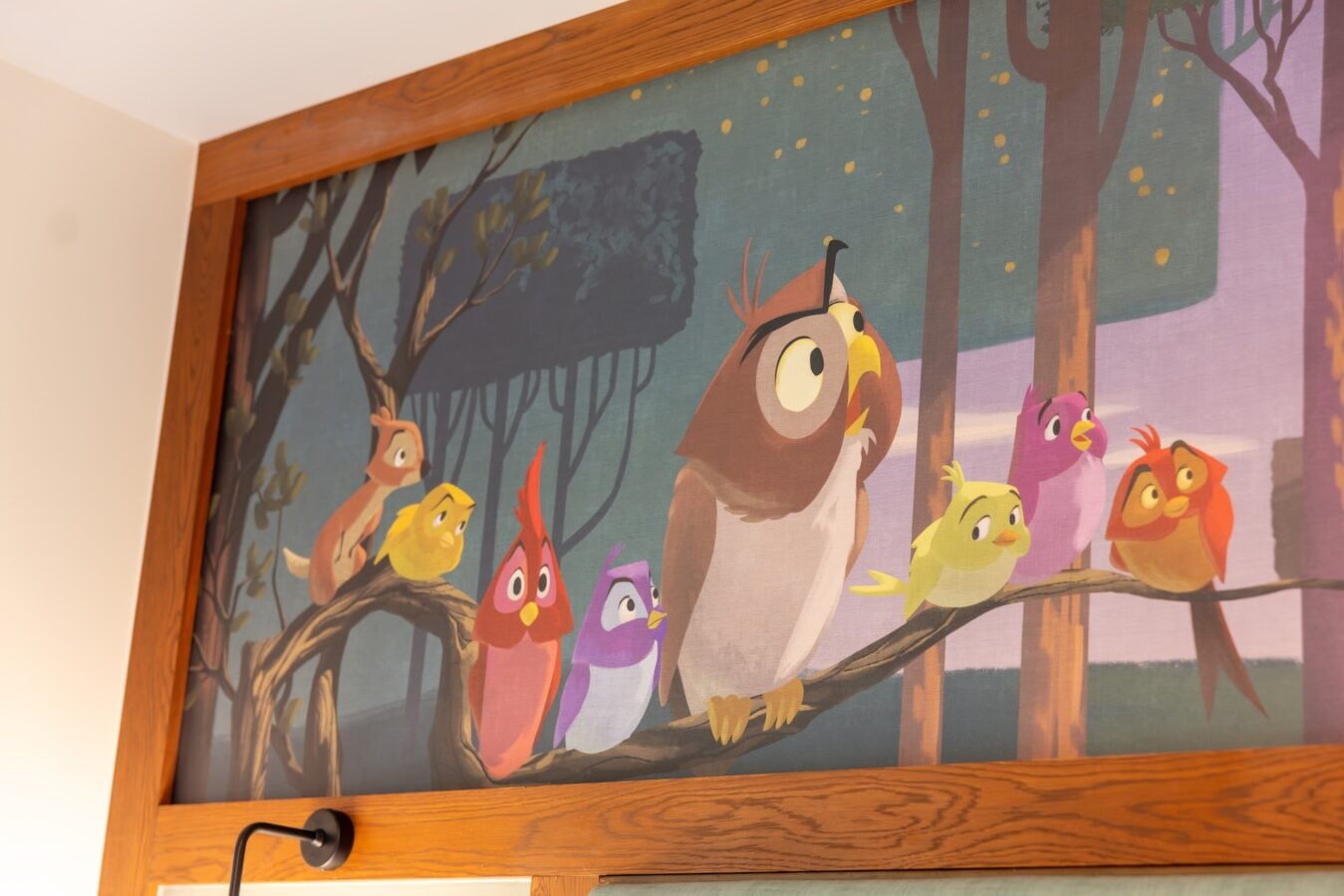 Colorful cartoon birds perched on tree branches in a framed mural on a wooden wall