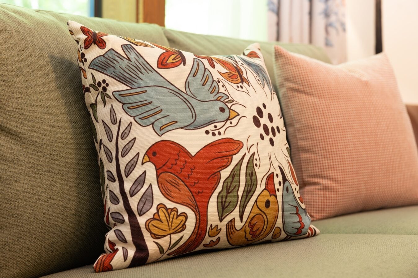 Colorful patterned throw pillow on a beige sofa with a pink checkered cushion in the background