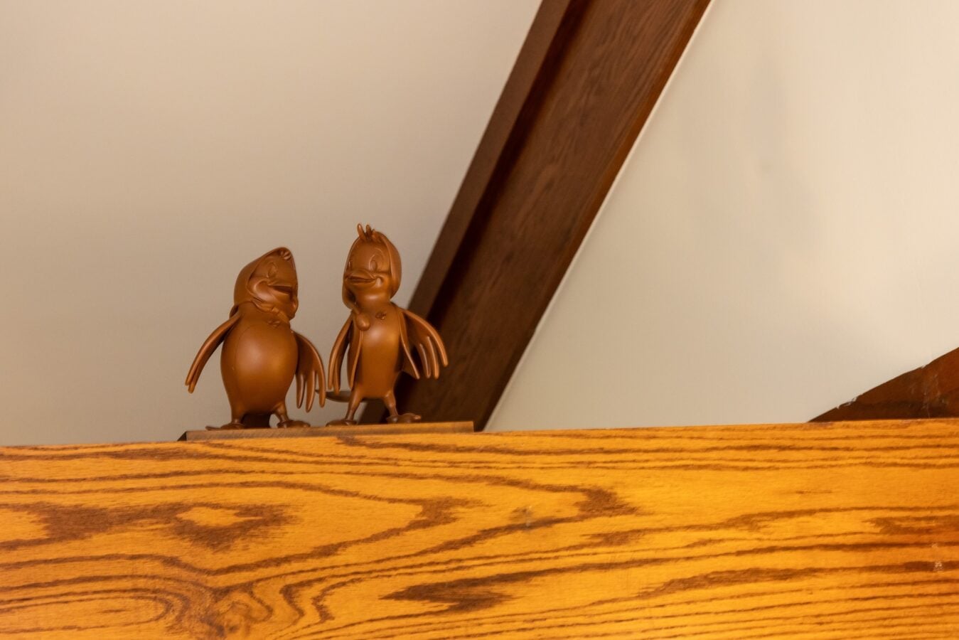 Two brown chocolate bunny figurines standing on a wooden shelf beneath a curved beam in warm light