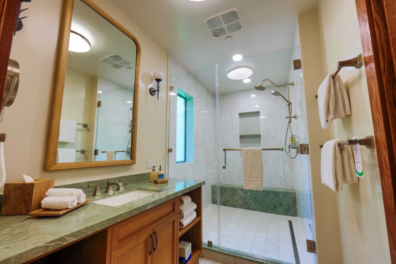 Bathroom with wood framed mirror green marble countertop towels and glass enclosed shower