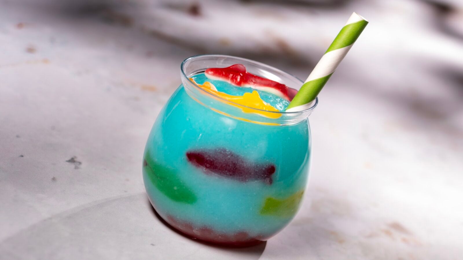 2026WDWCoolKidsSummerTreats4 Fantasy Land News Blue tropical cocktail in a rounded glass with a green and white striped straw and colorful red and yellow garnish outside the rim